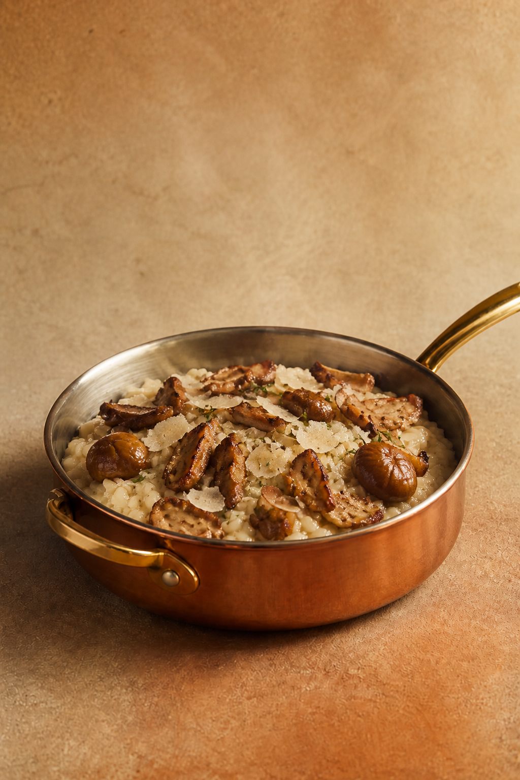 Risotto aux marrons et cèpes dans une casserole en cuivre, fond beige pierre
